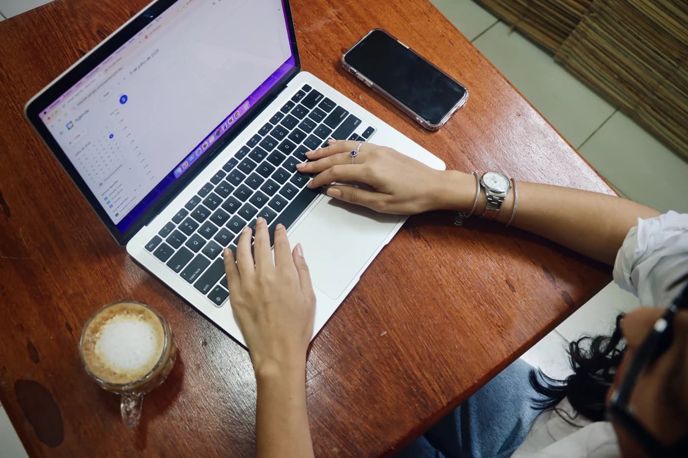 Isabella usando seu notebook à mesa de madeira, com uma xícara de café ao lado.